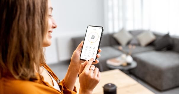 Young woman holding smart phone with launched security application at home. Concept of controlling and managing home security from a mobile device
