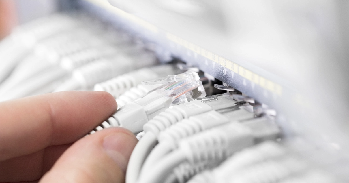 Close up of a tech's fingers as they put a network cable into a switch full of white cables.